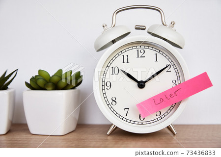 Procrastination and delay concept. Sticky note with word later on white alarm clock. Urgency time Procrastination and delay concept. Sticky note with word later on white alarm clock. Urgency time 73436833