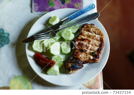 roasted steak meat with bone, cucumber , ketchup fork and knife 73437154
