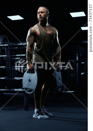 Tattooed male bodybuilder holding dumbbells. 73437337