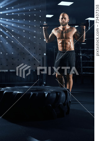 Shirtless man holding sledgehammer behind neck. Shirtless man holding sledgehammer behind neck. 73437338
