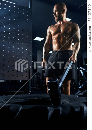Shirtless bodybuilder carrying sledgehammer in gym. Shirtless bodybuilder carrying sledgehammer in gym. 73437340
