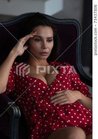 Alluring young woman in feminine dress resting in armchair Alluring young woman in feminine dress resting in armchair 73437806