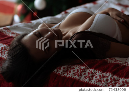 Alluring young lady relaxing on bed with closed eyes during Christmas holidays Alluring young lady relaxing on bed with closed eyes during Christmas holidays 73438006