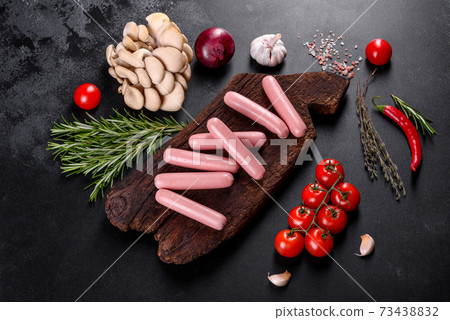 Boiled sausages on a wooden cutting board on a dark concrete background 73438832