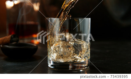 Glass of whisky with splashing liquid and ice rocks inside. Glass of whisky with splashing liquid and ice rocks inside. 73439395