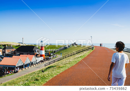 Westkapelle, The Netherlands, August 2019. The built-up area, below sea level, is protected by an artificial hill that surrounds it. On the top of the hill a red road. Westkapelle, The Netherlands, August 2019. The built-up area, below sea level, is protected by an artificial hill that surrounds it. On the top of the hill a red road. 73439862