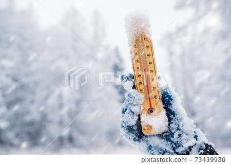 Human hand holding a thermometer with the low temperature against winter nature background with snowfall. Human hand holding a thermometer with the low temperature against winter nature background with snowfall. 73439980