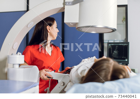 Extracorporeal Shock Wave Therapy. Kidney stone treatment. Side view of woman doctor looking at the digital screen of the lithotriptor to determine kidney stones position. Focus on female doctor Extracorporeal Shock Wave Therapy. Kidney stone treatment. Side view of woman doctor looking at the digital screen of the lithotriptor to determine kidney stones position. Focus on female doctor 73440041