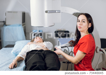 Treatment of urethral stones by non-invasive extracorporeal shock wave lithotripsy. Woman doctor working with modern lithotripter to crush kidney stones for her female patient in modern clinic Treatment of urethral stones by non-invasive extracorporeal shock wave lithotripsy. Woman doctor working with modern lithotripter to crush kidney stones for her female patient in modern clinic 73440045