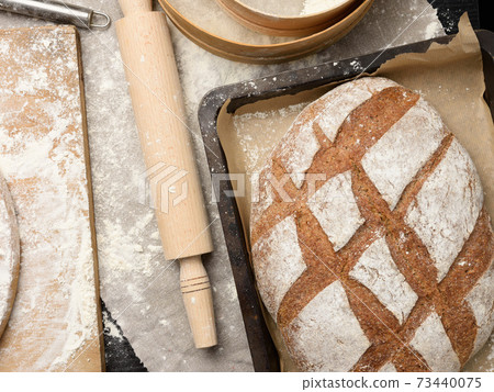 baked oval rye flour bread in a metal baking sheet on the table baked oval rye flour bread in a metal baking sheet on the table 73440075