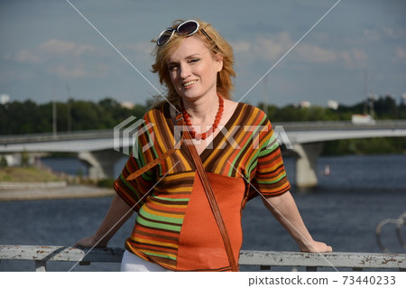 A woman in 1970-style clothes and sunglasses smiles outdoors A woman in 1970-style clothes and sunglasses smiles outdoors 73440233