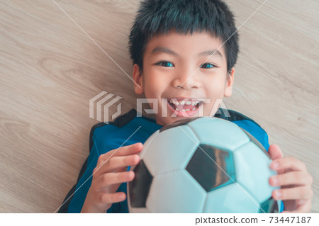 Happy Soccer Boy lying on wooden floor holding a soccer ball with copy space. Happy Soccer Boy lying on wooden floor holding a soccer ball with copy space. 73447187