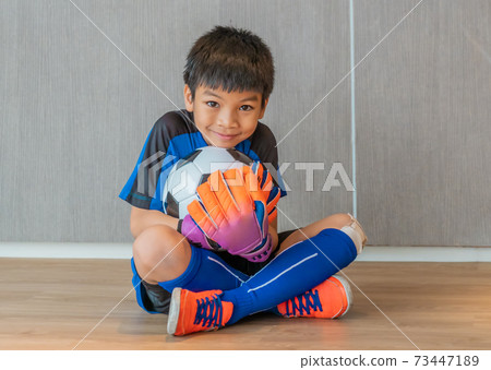 Asian boy is a football goalkeeper wearing gloves and holding a soccer ball with smile face. Asian boy is a football goalkeeper wearing gloves and holding a soccer ball with smile face. 73447189