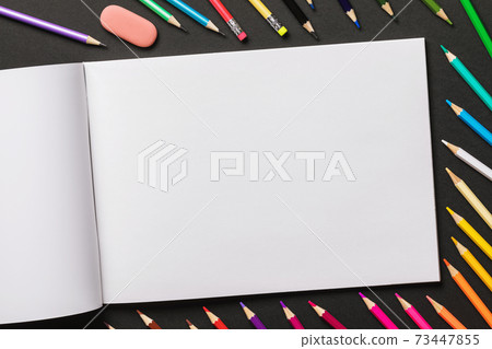 Various colored pencils and sketchbook on a black background with copy space 73447855