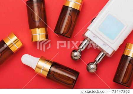 Gel and device for microcurrent stimulation of facial muscles on a red background, top view Gel and device for microcurrent stimulation of facial muscles on a red background, top view 73447862