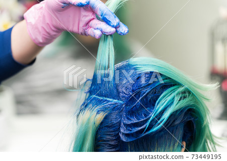 Hairdressers raise shock of blue hair of client during coloring process Hairdressers raise shock of blue hair of client during coloring process 73449195