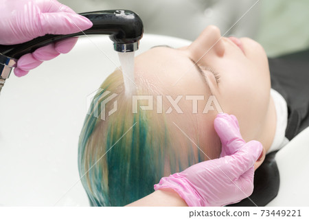 Hairdresser hands wash long hair of customer with green and discolored hair in sink with water from shower Hairdresser hands wash long hair of customer with green and discolored hair in sink with water from shower 73449221