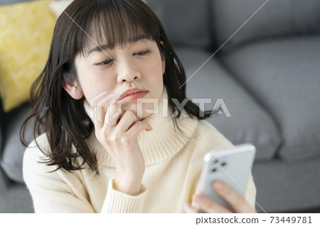 A young woman looking at a smartphone and thinking 73449781