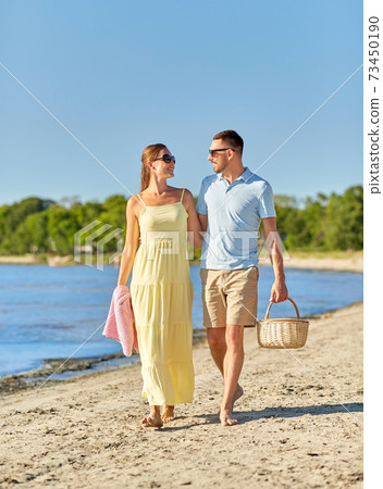 happy couple with picnic basket walking on beach 73450190