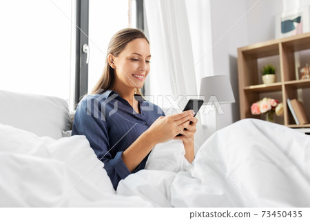 young woman with smartphone in bed in morning young woman with smartphone in bed in morning 73450435