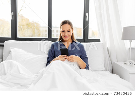 young woman with smartphone in bed in morning 73450436
