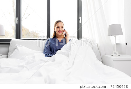 happy woman calling on smartphone in bed at home 73450438