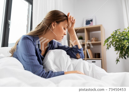 sleepy or stressed woman sitting in bed at home 73450453