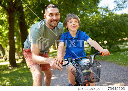 father teaching little son to ride bicycle at park 73450603