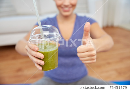 happy woman with cup of smoothie showing thumbs up 73451579