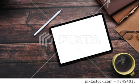 Top view of vintage workspace with mock up digital tablet with blank screen, coffee cup and notebook on wooden table. Top view of vintage workspace with mock up digital tablet with blank screen, coffee cup and notebook on wooden table. 73454013