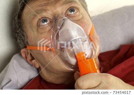 Sick senior adult man breathing through oxygen mask, rolling his eyes. Treatment of asthma, allergies, bronchitis, pneumonia in Covid19 and respiratory diseases. Selective focus. Sick senior adult man breathing through oxygen mask, rolling his eyes. Treatment of asthma, allergies, bronchitis, pneumonia in Covid19 and respiratory diseases. Selective focus. 73454017