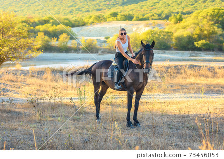 Girl with glasses strokes a horse riding in the autumn forest 73456053