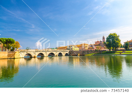 Famous stone arch Tiberius bridge Ponte di Tiberio Augustus over Marecchia river water, old buildings houses in historical touristic city centre Rimini Famous stone arch Tiberius bridge Ponte di Tiberio Augustus over Marecchia river water, old buildings houses in historical touristic city centre Rimini 73457140
