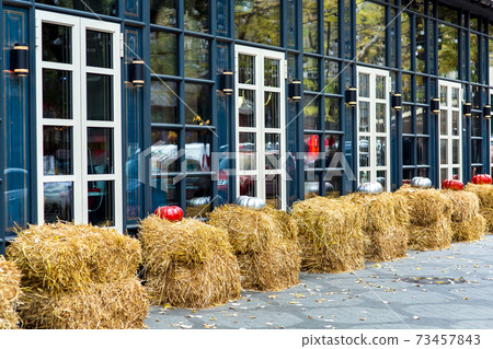 The facade of the building with windows with lanterns and haystacks near the building and taverns for the autumn holiday Halloween. The facade of the building with windows with lanterns and haystacks near the building and taverns for the autumn holiday Halloween. 73457843