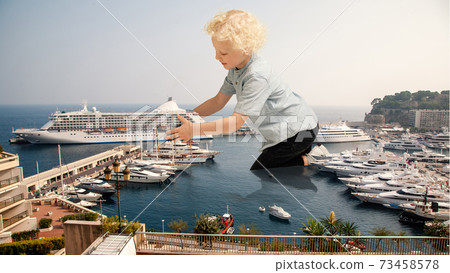 See the world by children's eyes - little cute curly boy playing with big liner ship sitting on the city See the world by children's eyes - little cute curly boy playing with big liner ship sitting on the city 73458578