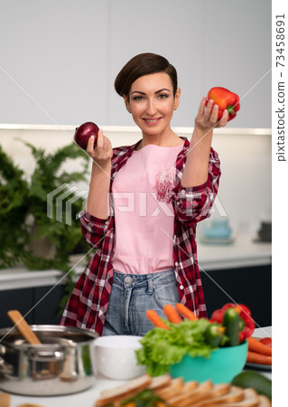 Holding apples in the hands housewife wearing plaid shirt with a short hairstyle while cooking apple pie standing at the kitchen. Healthy food at home Holding apples in the hands housewife wearing plaid shirt with a short hairstyle while cooking apple pie standing at the kitchen. Healthy food at home 73458691