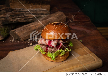 Fresh craft beef burger with fried slices of bacon and cherry sauce, fresh lettuce next to the decorative wooden lodges. Restaurant concept. Street food concept 73458692