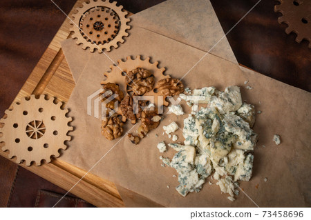 Top view of a blue cheese or bleu cheese served with walnuts on food wrapping paper and chalkboard with decorative wooden details of a simple mechanism. Cheese with the mold Top view of a blue cheese or bleu cheese served with walnuts on food wrapping paper and chalkboard with decorative wooden details of a simple mechanism. Cheese with the mold 73458696