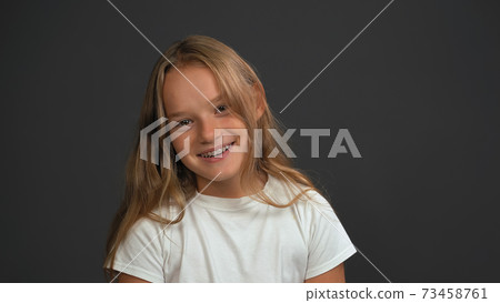 Smiling girl with bow sideways head looking at the camera wearing white t-shirt isolated on dark grey or black background. Child emotions concept 73458761