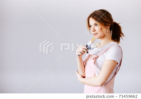 A woman in a pink in work clothes on a gray background is looking at the camera. A woman in a pink in work clothes on a gray background is looking at the camera. 73459662