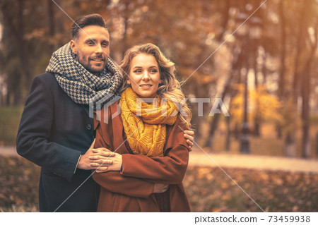 Couple in love man and a woman hugged from behind smile looking at their kids in the autumn park. Outdoor shot of a young couple in love having great time. Autumn toned image Couple in love man and a woman hugged from behind smile looking at their kids in the autumn park. Outdoor shot of a young couple in love having great time. Autumn toned image 73459938