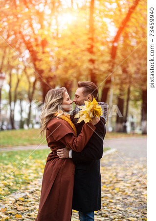 Husband and a wife hugged smile looking at each other in the autumn park. Half-length portrait of a kissing young couple. Outdoor shot of a young couple in love in a autumn park 73459940