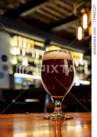 Glass of stout beer on wooden table in warm light of bar Glass of stout beer on wooden table in warm light of bar 73460127