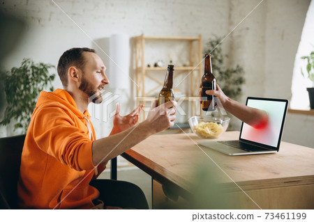 Young man drinking beer during meeting friends on virtual video call. Distance online meeting, chat together on laptop at home. 73461199