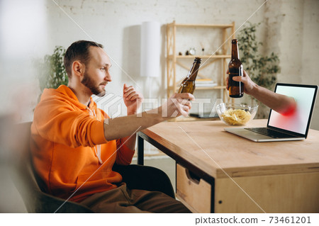 Young man drinking beer during meeting friends on virtual video call. Distance online meeting, chat together on laptop at home. 73461201