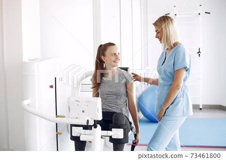 Young woman doing exercises on simulator with therapist in gym 73461800