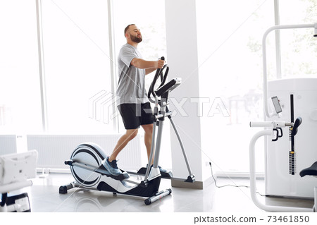 Bearded man using spin bike in physiotherapy room Bearded man using spin bike in physiotherapy room 73461850