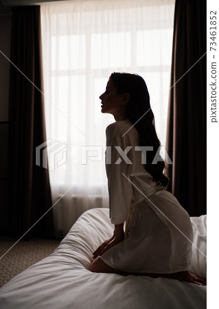 silhouette. beautiful woman with makeup, long hair sits in white robe on bed silhouette. beautiful woman with makeup, long hair sits in white robe on bed 73461852