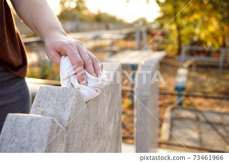 Cleaning cemetery. A woman's hand washes grey monument at grave with rag. Cleaning cemetery. A woman's hand washes grey monument at grave with rag. 73461966