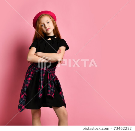 Ginger teenage kid in black dress, checkered shirt, red hat and choker. Smiling, hands foled, posing on pink background. Close up Ginger teenage kid in black dress, checkered shirt, red hat and choker. Smiling, hands foled, posing on pink background. Close up 73462252